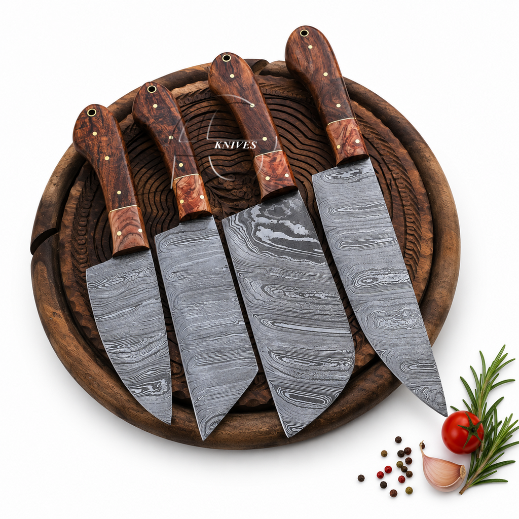 Four Damascus steel kitchen knives with patterned steel blades and reddish-brown wooden handles, arranged on a round wooden cutting board with small food props in the corner.