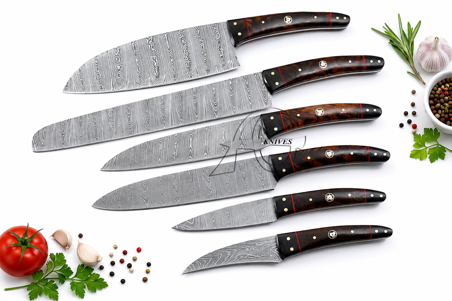 A set of seven Damascus steel kitchen knives with dark brown wooden handles and brass bolsters, arranged diagonally on a white background with culinary props like a tomato, garlic, peppercorns, and rosemary.