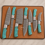 Seven custom kitchen knives with patterned steel blades and turquoise handles are arranged on a brown leather knife block over a white marble surface.