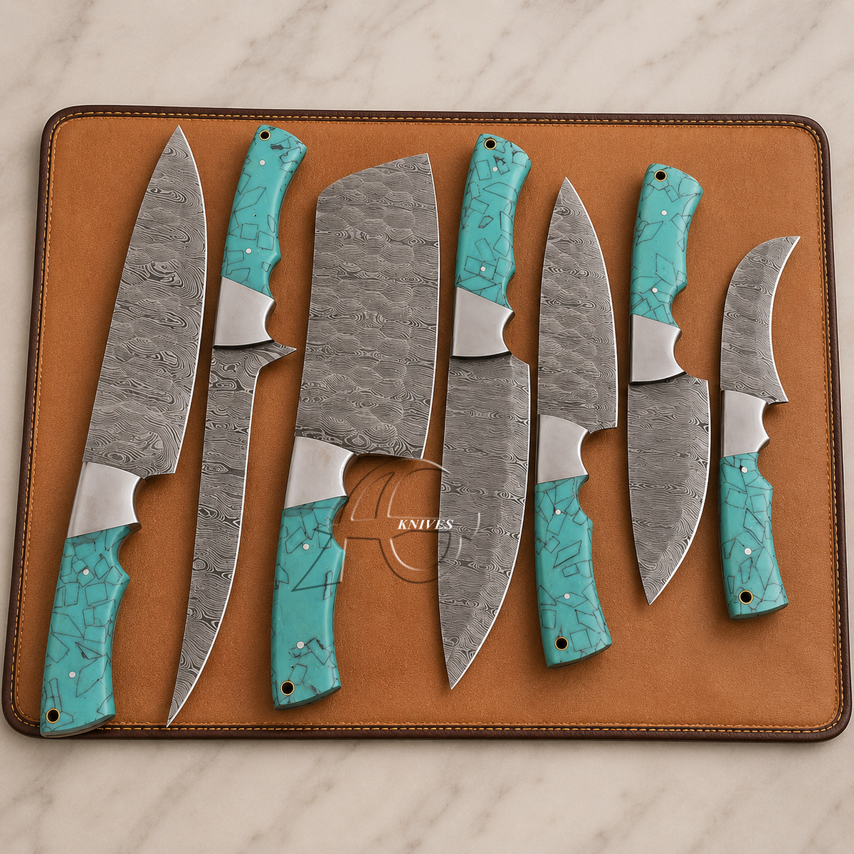 Seven custom kitchen knives with patterned steel blades and turquoise handles are arranged on a brown leather knife block over a white marble surface.