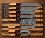 A set of eight kitchen knives with Damascus steel blades and wooden handles with red inlays, arranged diagonally on a wooden cutting board with an American flag star pattern.