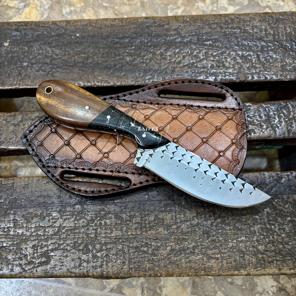 A fixed-blade knife with a dark wood handle and a patterned silver blade rests on a brown leather sheath over a weathered wooden surface.