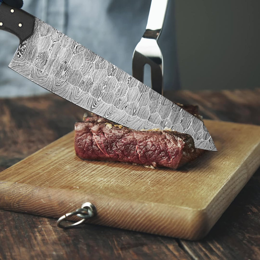 A close-up of a high-end kitchen knife with a Damascus steel pattern blade slicing a piece of raw beef on a wooden cutting board, with a carving fork behind it.