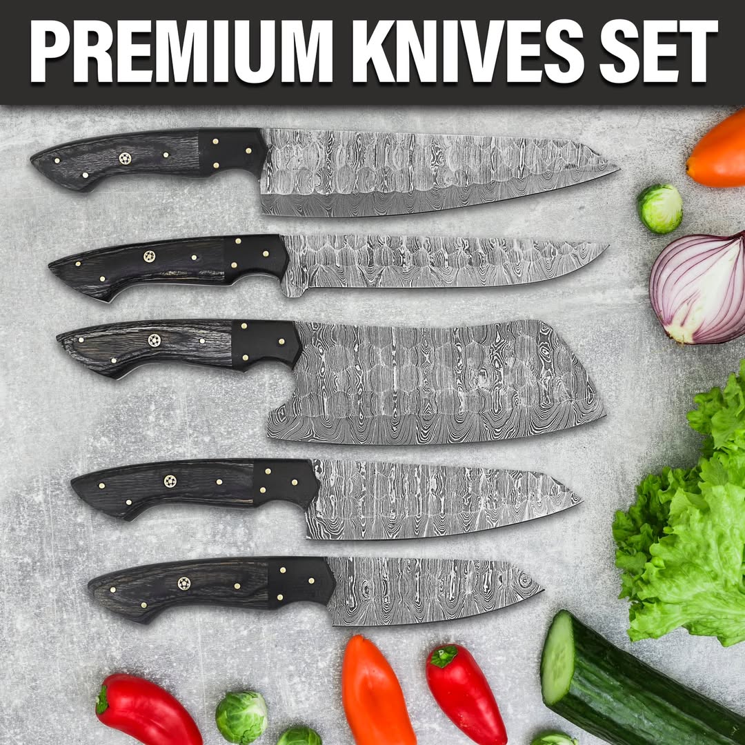 A premium 5-piece kitchen knife set with patterned Damascus steel blades and black handles, arranged on a gray stone surface with fresh vegetables like lettuce, cucumber, red peppers, and onions. A black banner at the top reads 'PREMIUM KNIVES SET' in bold white letters.
