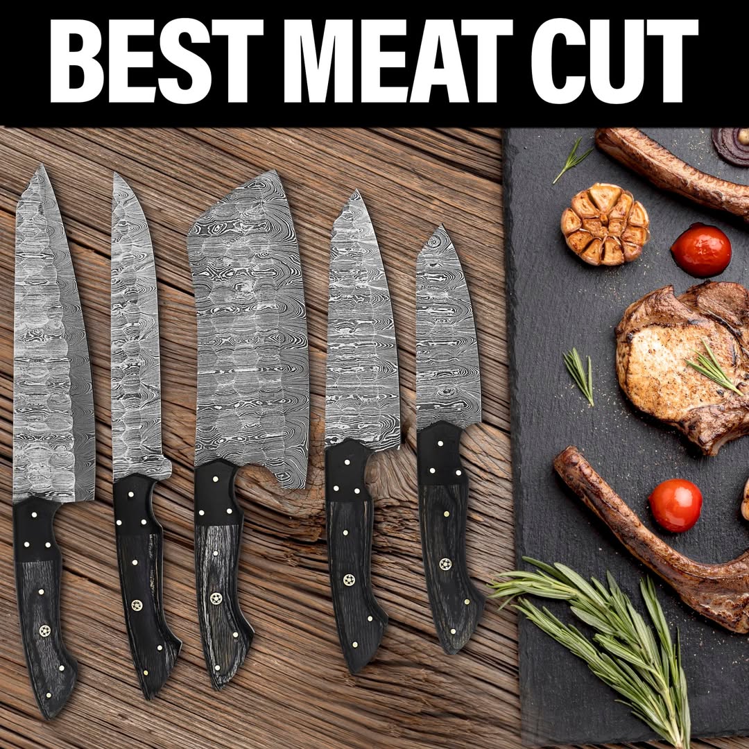 A set of five damascus steel kitchen knives with black handles arranged on a wooden surface next to cooked meat and vegetables on a dark slate board, with the text 'BEST MEAT CUT' across the top.