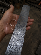 Hand holding a Damascus steel knife blade with a blurred background