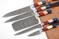 Five Damascus steel kitchen knives with colorful handles in red, cream, and blue, arranged diagonally on a brown leather knife roll against a white background.