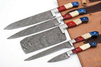 Five Damascus steel kitchen knives with colorful handles in red, cream, and blue, arranged diagonally on a brown leather knife roll against a white background.