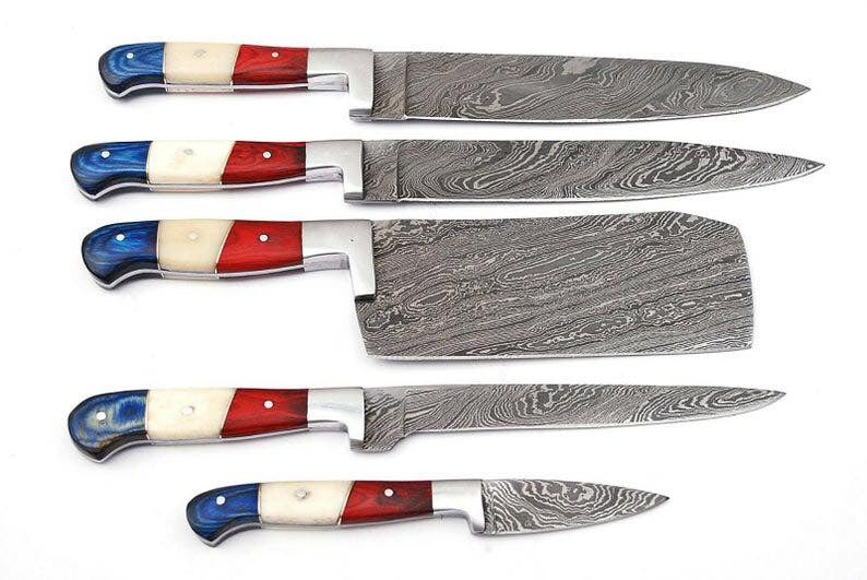 Five Damascus steel kitchen knives with colorful handle scales in blue, red, and cream, arranged vertically on a plain white background.