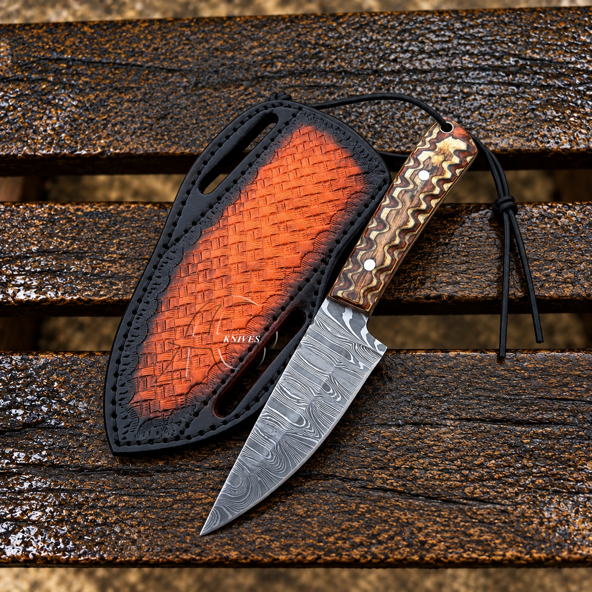 A Damascus steel fixed-blade knife with a patterned wood handle and black cord lanyard, displayed next to its black sheath with a textured orange-red interior, set on a weathered wooden plank surface.