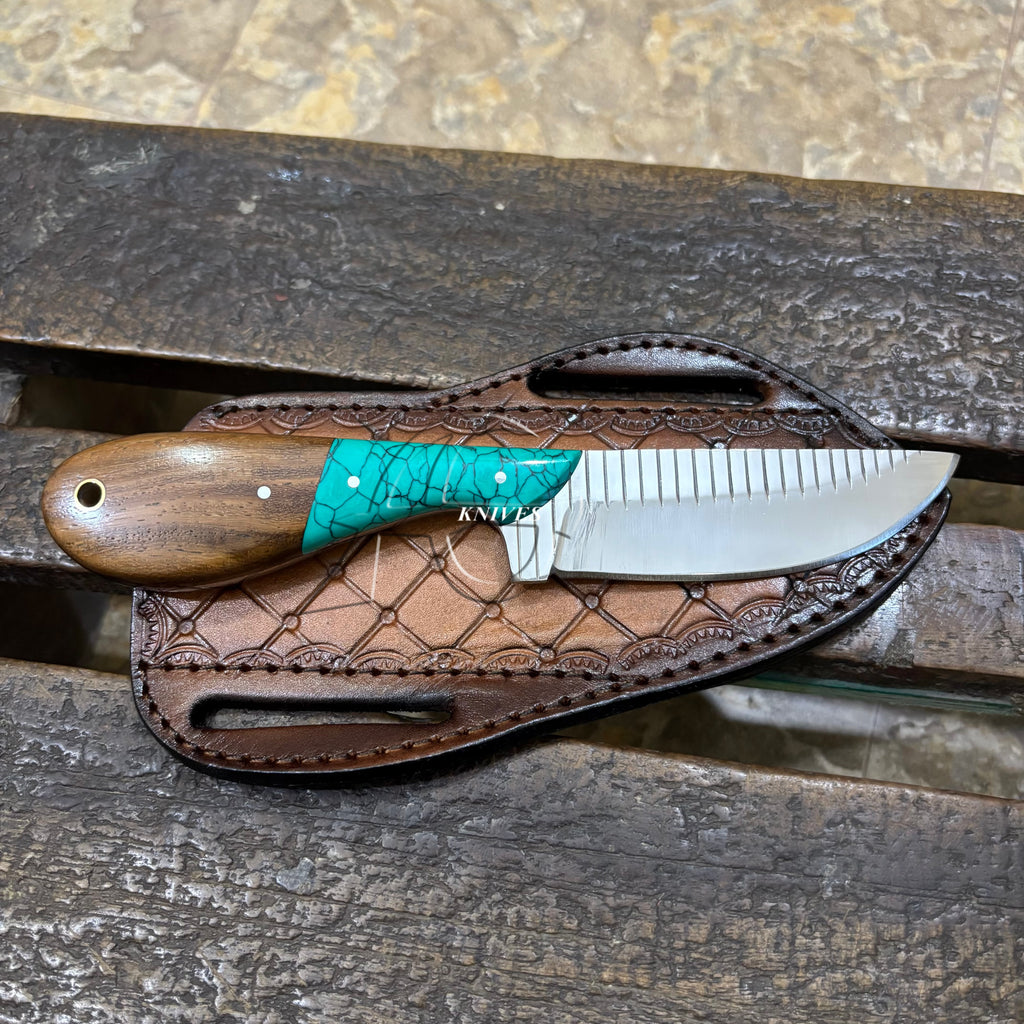 A fixed-blade knife with a brown wooden handle and turquoise inlay rests on a brown leather sheath over a weathered wooden surface.