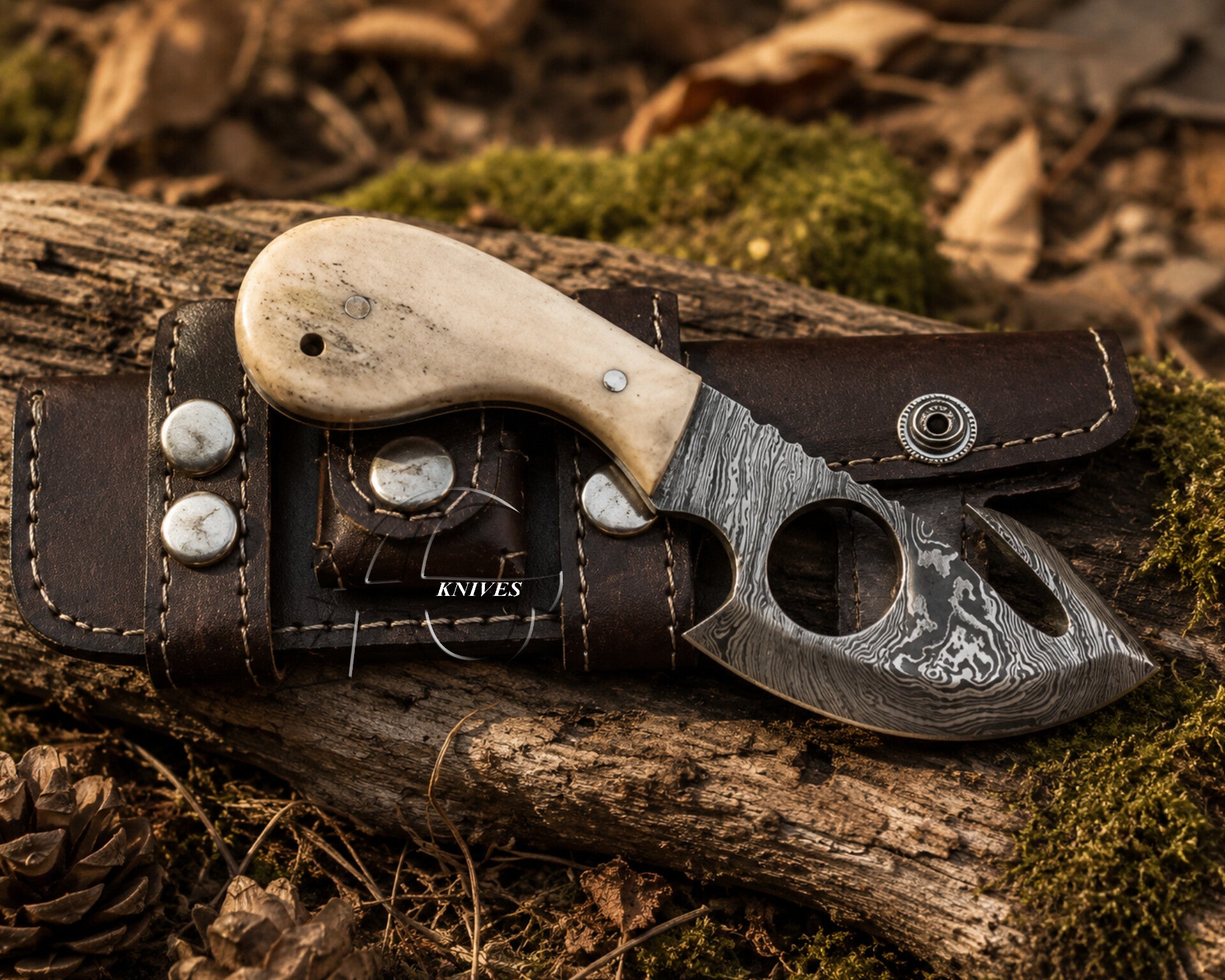 A fixed-blade knife with a patterned steel blade and an off-white handle, resting on a dark brown leather sheath over a log outdoors.