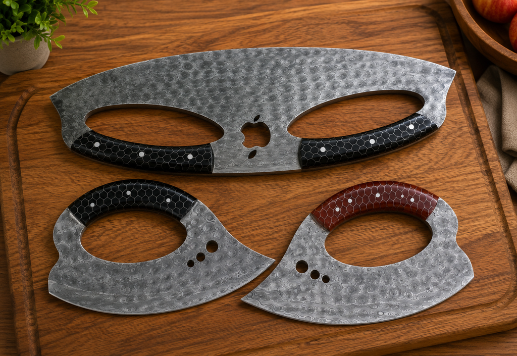 Three Hand Forged Ulu & Mezzaluna Kitchen Knife Set curved metal knife blade covers or guards with oval cutouts, arranged on a wooden cutting board. Two have black textured handles with silver rivets, and one has a reddish-brown textured handle with silver rivets.