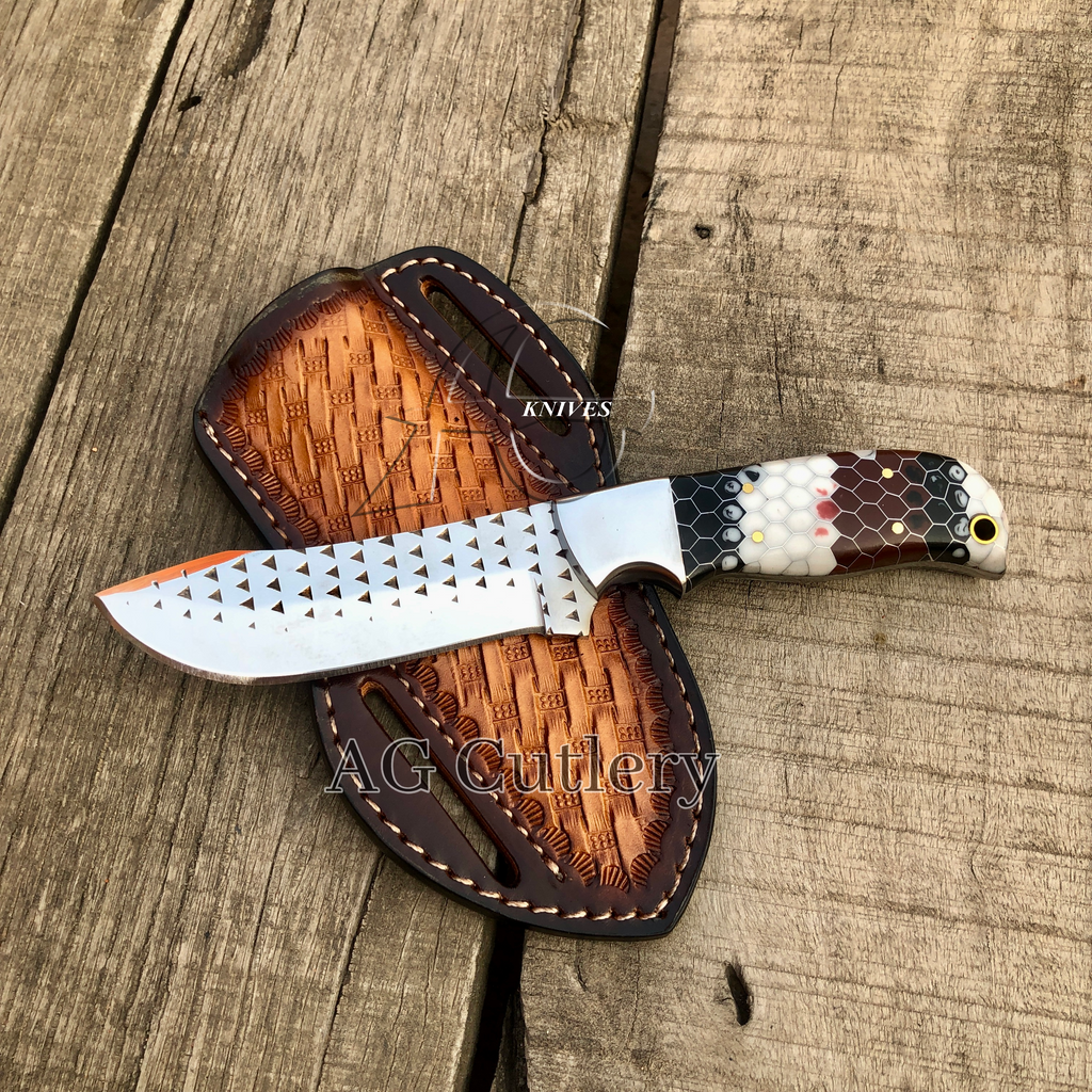 A custom fixed-blade knife with a patterned silver blade and a multi-colored honeycomb handle, displayed diagonally on its brown leather sheath over a rustic wooden plank background.