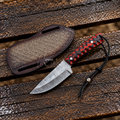 A fixed-blade knife with a patterned steel blade, red and black handle scales, and a black cord lanyard, shown beside a matching textured brown sheath on a weathered wooden surface. The brand name 'NANOS' is visible on the sheath.