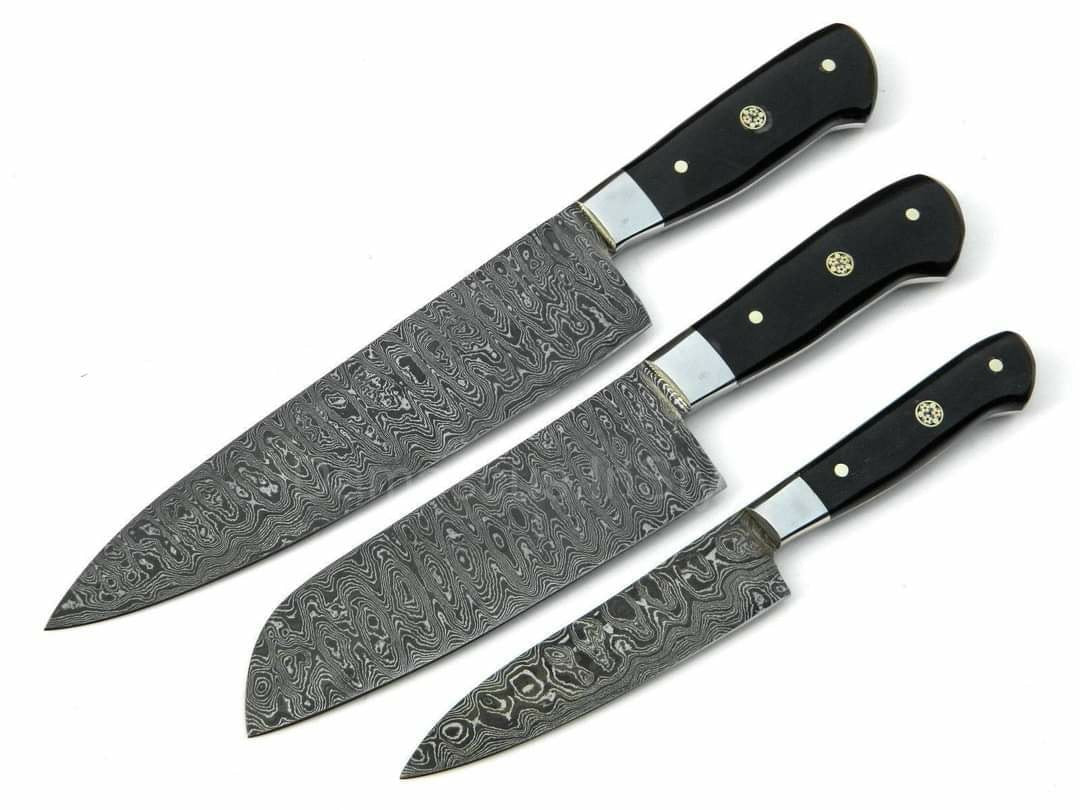 Three kitchen knives with patterned Damascus steel blades and black handles, arranged diagonally on a plain white background.