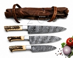 Three Damascus steel chef knives with patterned handles are displayed below a brown leather knife sheath on a white background, with small food props including a tomato, onion, peppercorns, and parsley at the bottom right.