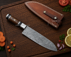 A Damascus steel chef's knife with a patterned steel blade and a dark wood handle, displayed next to its brown leather sheath on a dark wooden cutting board with food props.