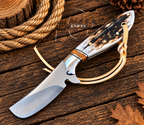 A fixed-blade knife with a satin-finished silver blade, a brown and black patterned horn handle, and a tan leather lanyard, displayed on a rustic dark wood surface with rope and autumn leaves.