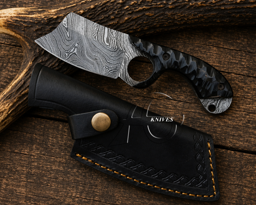 A fixed-blade knife with a patterned Damascus-style blade and a black textured handle, shown with a black sheath on a rustic wood surface with antlers.