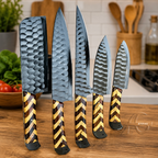 Five kitchen knives with hammered steel blades and striped wood handles are arranged upright on a wooden countertop in a kitchen setting.