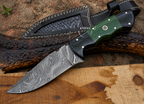 A fixed-blade knife with a patterned steel blade, black handle, and green textured grip, shown alongside a black sheath on a rustic wood and bark surface.