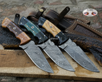 Four fixed-blade knives with patterned Damascus steel blades are arranged on a wooden board with leather sheaths. The handles feature different materials: wood, dark green inlay, black resin, and natural wood.