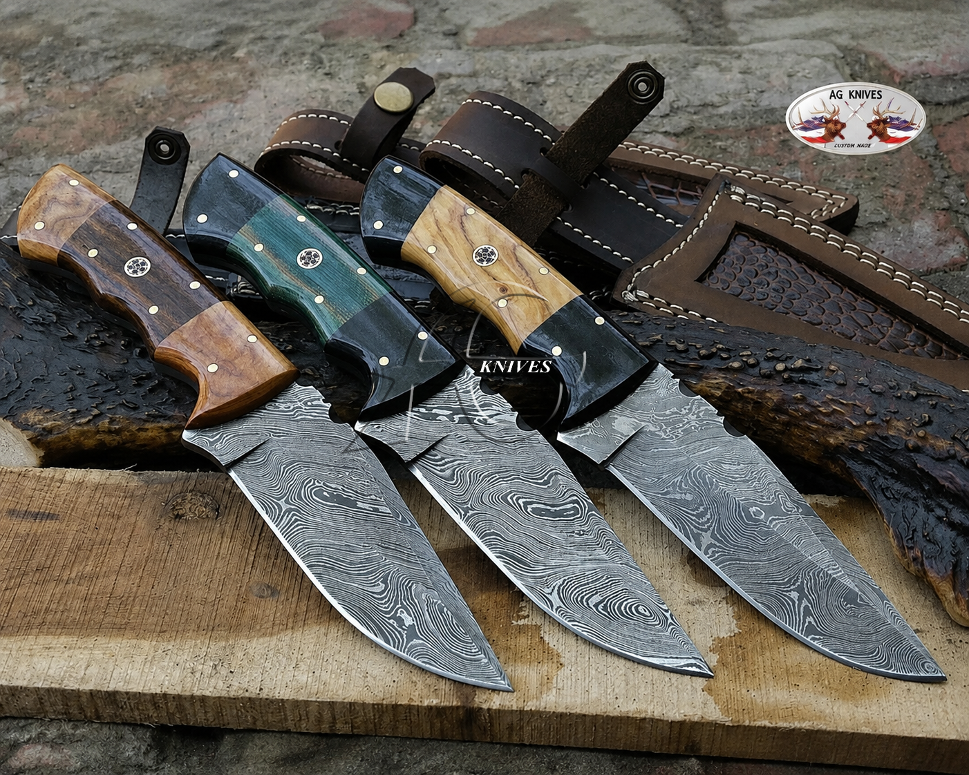 Four fixed-blade knives with patterned Damascus steel blades are arranged on a wooden board with leather sheaths. The handles feature different materials: wood, dark green inlay, black resin, and natural wood.