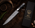 A Damascus steel chef's knife with a patterned steel blade and a black handle with silver accents, displayed diagonally next to its black gift box with gold 'AG Cutlery' branding. The scene is styled on a dark brown textured fur background with rustic props including a horn, rosemary, garlic, and peppercorns.
