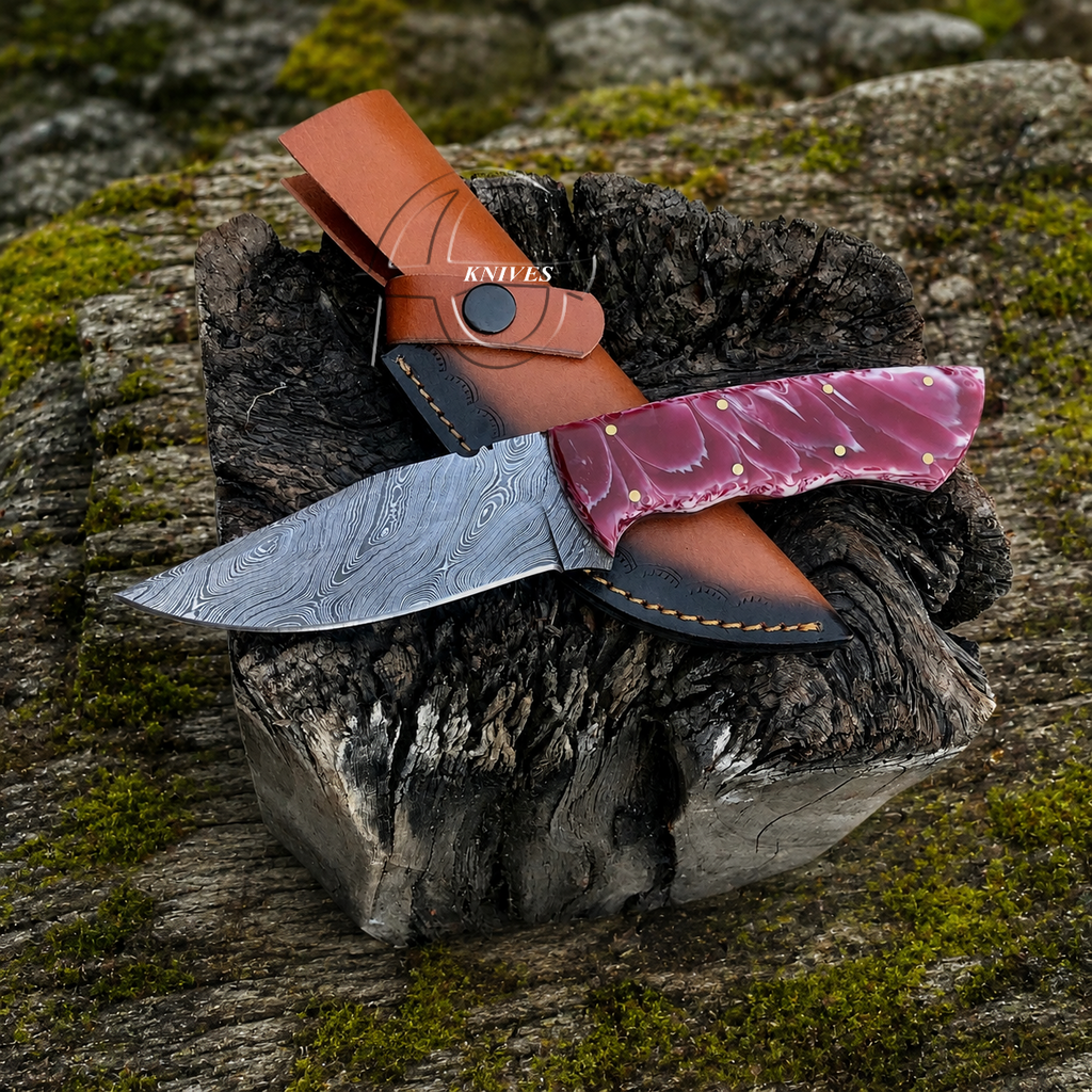 A fixed-blade knife with a patterned steel blade, a pink marbled handle, and a brown leather sheath, displayed on a mossy log outdoors.