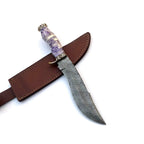 A fixed-blade knife with a patterned steel blade, a purple marbled handle, and a brown leather sheath, displayed on a clean white background.