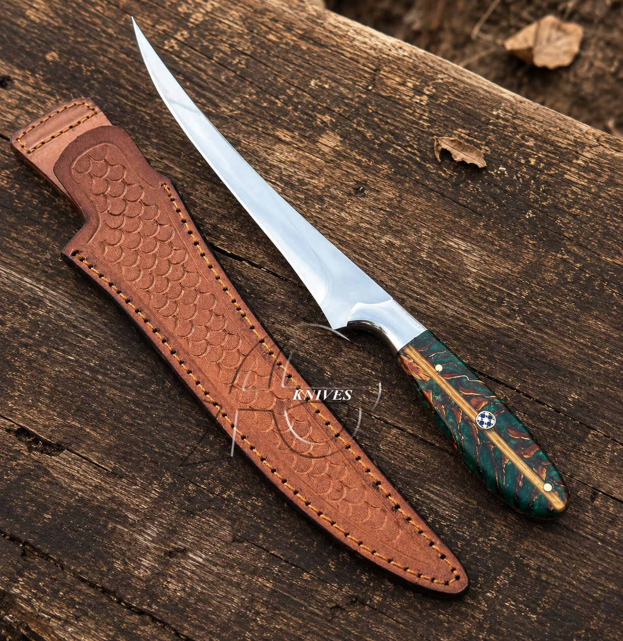 A fixed-blade knife with a polished silver blade and a green marbled handle with gold accents, shown next to its brown leather sheath on a rustic wooden surface.