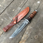 A fixed-blade knife with a patterned steel blade, a brown wrapped handle, and a brown leather sheath, displayed diagonally on a weathered wooden surface.