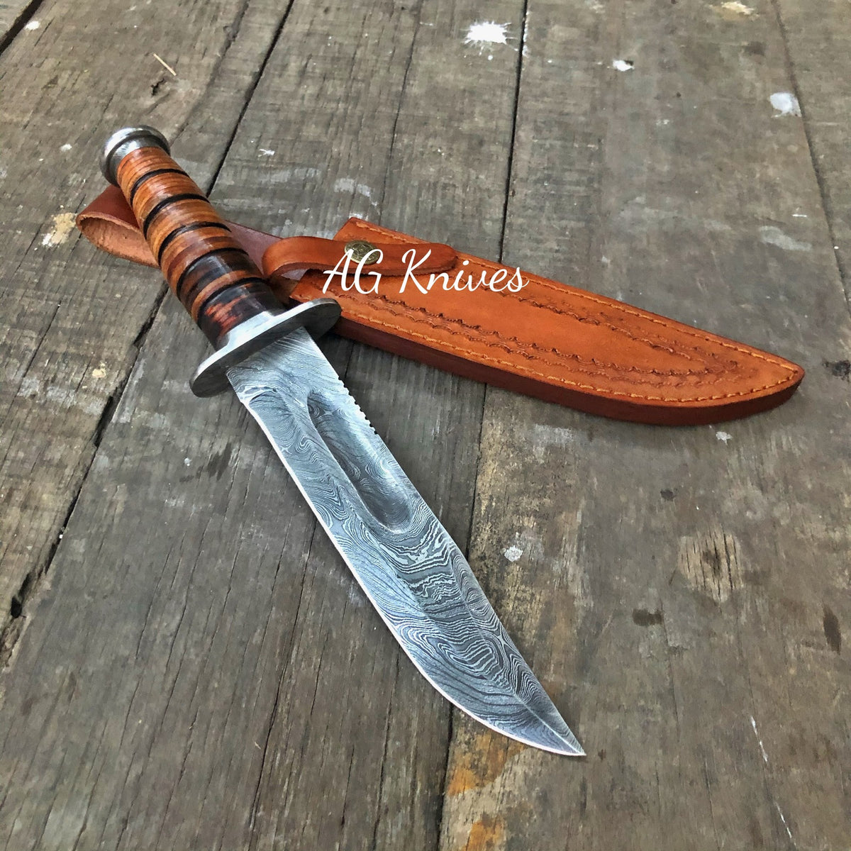 Decorative knife with a leather sheath on a wooden surface, branded 'AG Knives'.