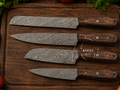 Set of four Damascus steel knives on a wooden cutting board with vegetables around.