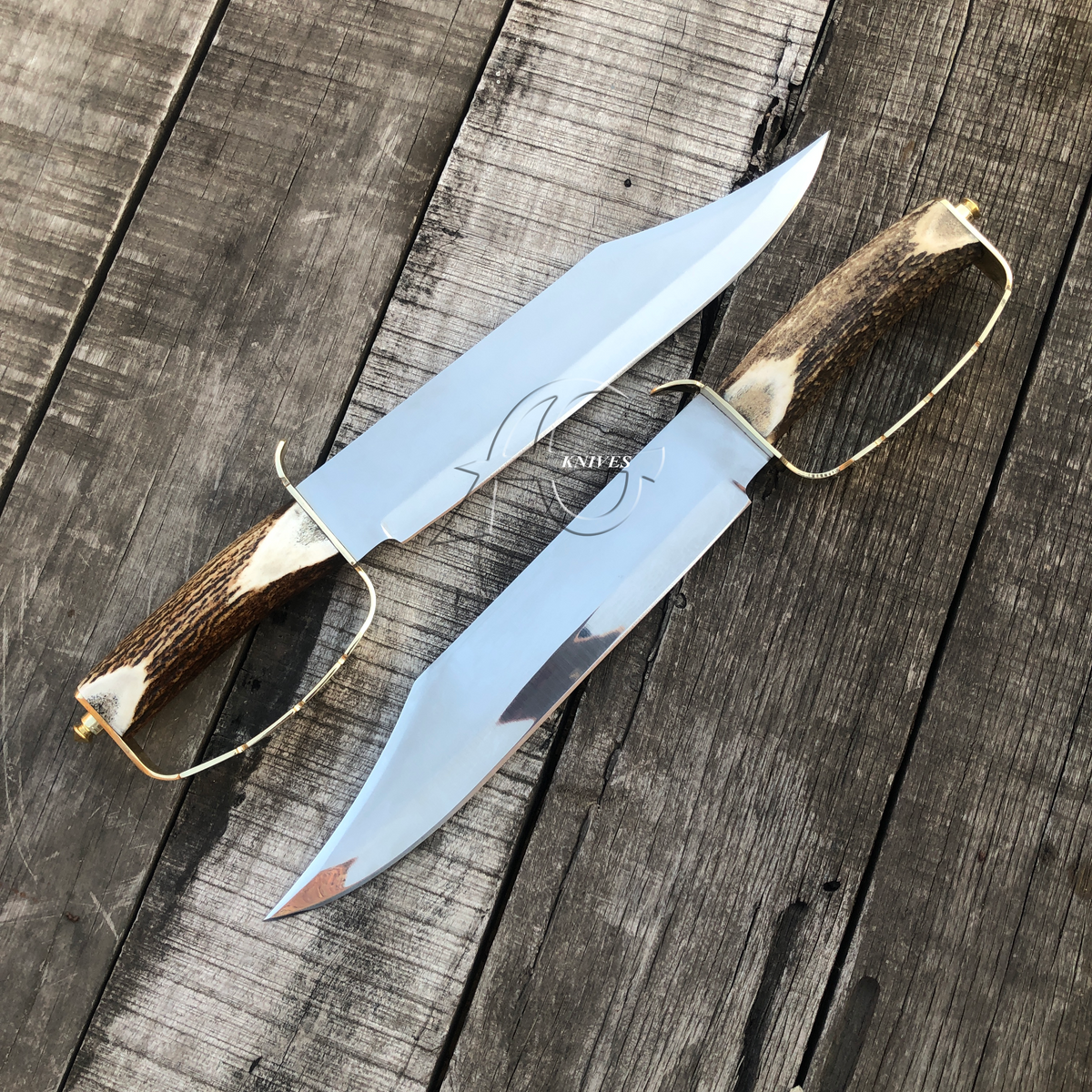 Two custom hunting knives with polished steel blades and antler handles, displayed diagonally on a weathered wooden plank surface. The brand name 'KAVU' is printed on the blades.