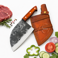 A large chef's knife with a dark textured steel blade and an orange-brown wooden handle lies next to a brown leather sheath on a white background, surrounded by food props including raw meat, parsley, red onion, cucumber, tomato, and peppercorns. A semi-transparent 'KNIVES' watermark is visible across the center.