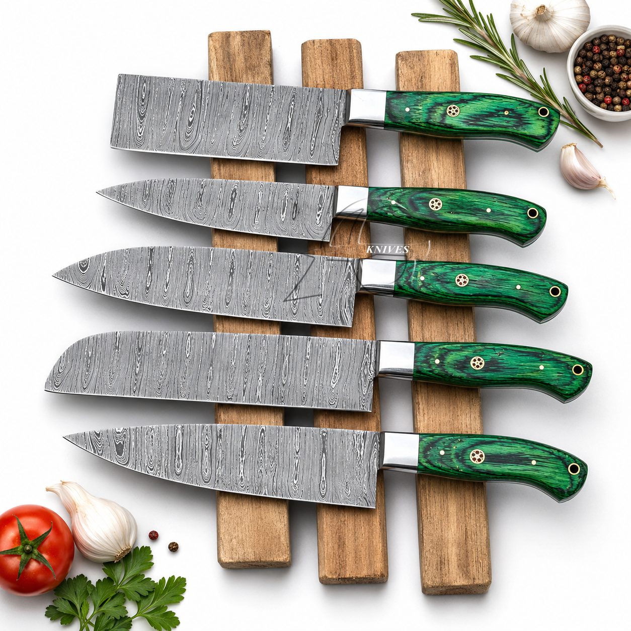 Five kitchen knives with patterned steel blades and glossy green handles are arranged on a wooden stand over a white background, styled with tomatoes, garlic, peppercorns, rosemary, and parsley.