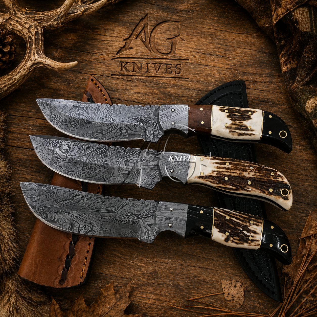 Three fixed-blade knives with patterned steel blades and mixed bone/bone-look handles are arranged on a rustic wood surface with a leather sheath and antler props. The engraved logo 'AG Knives' is visible above.