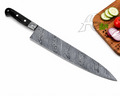A chef's knife with a patterned Damascus steel blade and a black handle, shown diagonally on a white background with a wooden cutting board and sliced vegetables in the top right corner.
