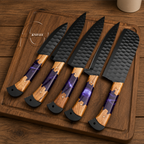 Five kitchen knives with hammered black blades and purple marbled handles resting on a wooden cutting board over a wooden table.