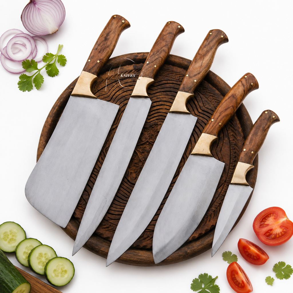 Four kitchen knives with silver blades and brown wooden handles arranged on a round dark wooden board, with sliced onions, cucumber, tomato, and cilantro placed around it on a white background.
