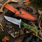 A fixed-blade knife with a patterned steel blade and a green marbled handle is displayed next to its brown leather sheath on a rustic wood surface with deer antlers, leaves, and binoculars.