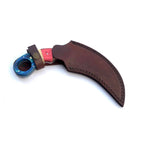 A curved knife with a blue star-patterned handle and a reddish-pink grip, shown with a brown leather sheath on a plain white background.
