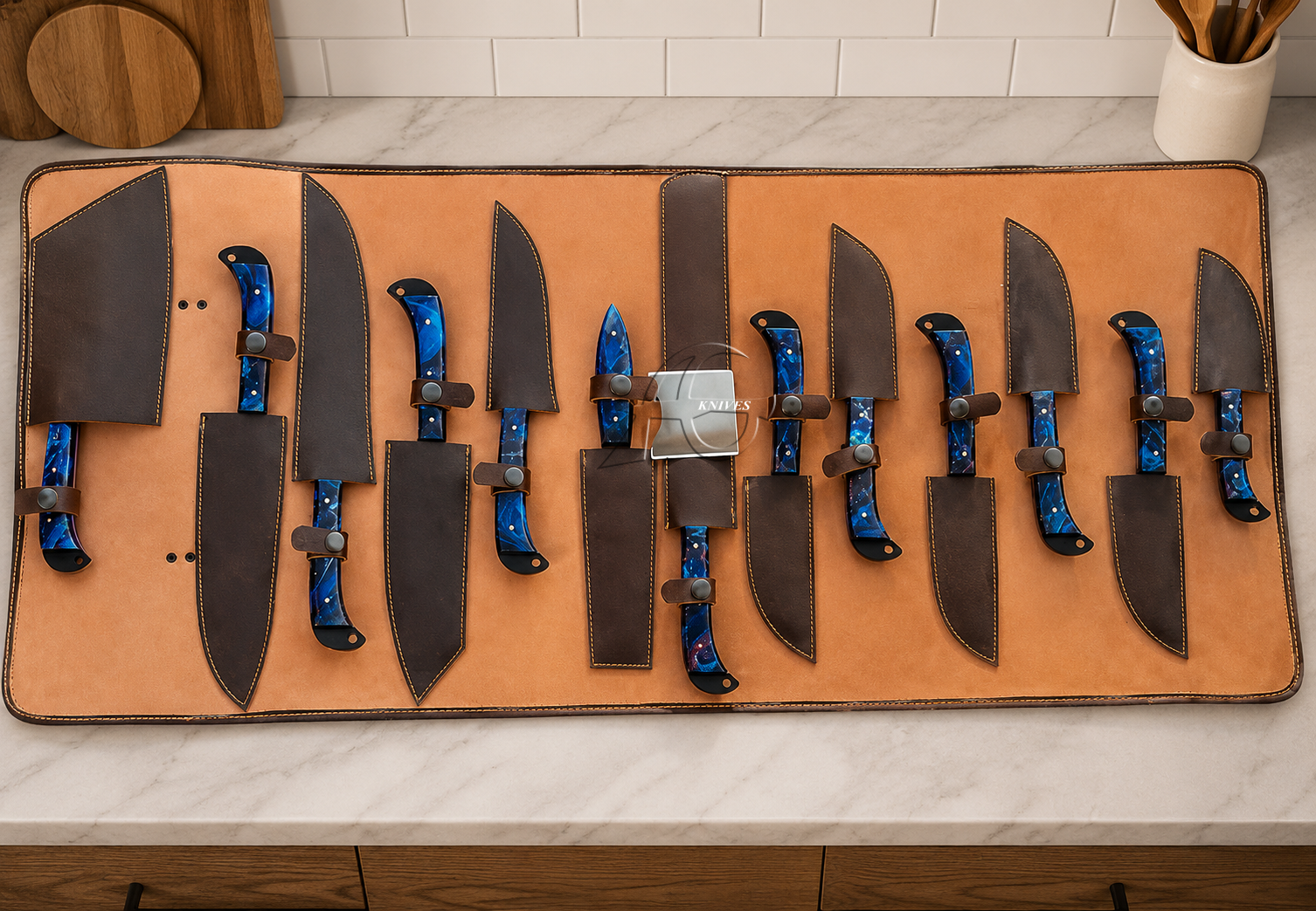 A set of ten kitchen knives with blue galaxy-patterned handles and dark brown leather sheaths, arranged on a tan leather knife roll over a white marble countertop.