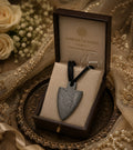 A Damascus steel arrowhead pendant necklace displayed inside an open dark brown presentation box with a beige insert. The box lid is printed with the text 'DAMASCUS STEEL' and 'Timeless.